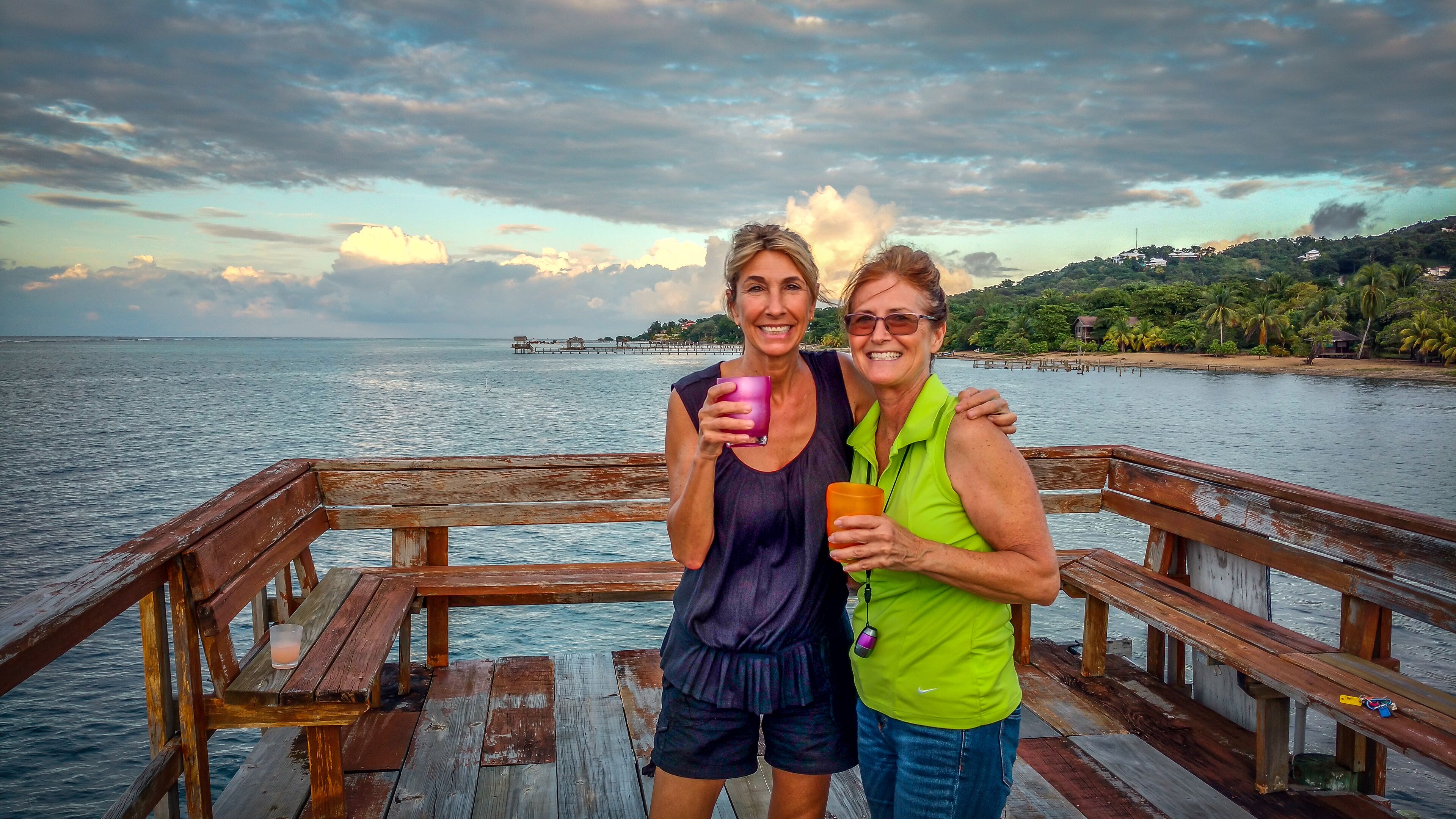 Two people on a wooden pier with a view of the sea and a distant island.