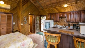 A cozy cabin with a wooden interior, a bed with floral bedding, a kitchen with wooden cabinets, and a large water dispenser.
