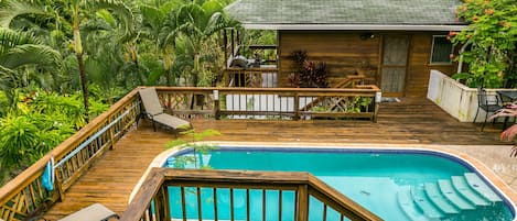 Una terraza de madera con piscina, rodeada de exuberante vegetación.