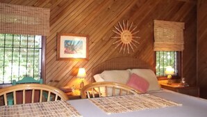 A cozy room with a wooden ceiling, a bed with a white mattress and pink pillow, a framed picture on the wall, and a sun-shaped decoration.