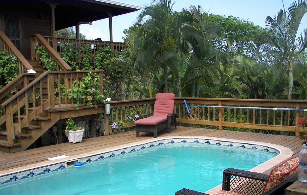 A swimming pool with a wooden deck, a red chair, and a staircase leading to a covered area.