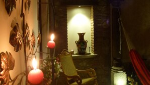 Una stanza poco illuminata con una parete in pietra, una sedia a dondolo in legno e un elemento decorativo in metallo.