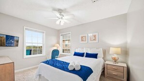 Ein ordentlich eingerichtetes Schlafzimmer mit einem großen Bett, zwei Nachttischen, einem Deckenventilator und Blick ins Freie durch ein Fenster.