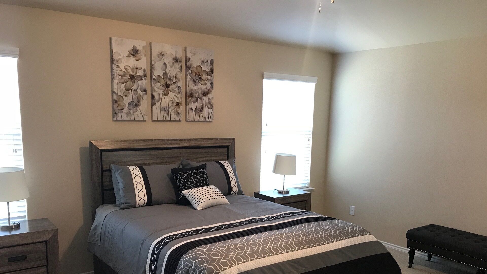 Et soveværelse med seng, sengeborde, lampe og et kunstværk på væggen.