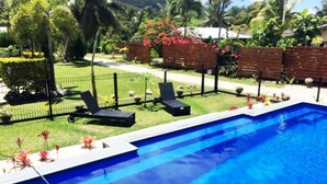 A swimming pool with two lounge chairs, surrounded by a well-maintained garden and a brick wall. - Great Value steps from Muri Beach with Kayaks, Paddle Boards, Pool, Free WIFI ! (Muri Beach)