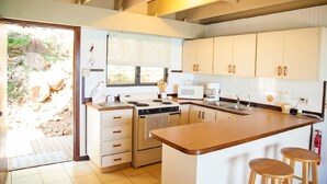 A modern kitchen with white cabinets, a central island with stools, a microwave, a stove, and a sink. - Punta Aloe 20 Ocean Front Villa Apartment (Culebra)