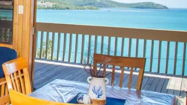 A wooden deck with a table and chairs, overlooking a body of water and a distant landmass. - Punta Aloe 20 Ocean Front Villa Apartment (Culebra)