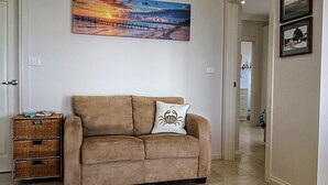 A beige sofa with a crab pillow, a wicker basket, and a sunset painting on the wall. - SeaChange Sceale Bay (Sceale Bay)