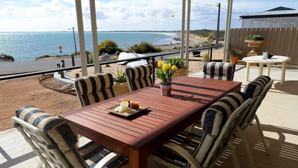 An outdoor patio with a wooden table and striped chairs, overlooking a beach and ocean. - SeaChange Sceale Bay (Sceale Bay)