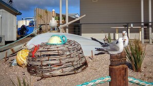 A coastal scene with a bird feeder, a lobster trap, and a sailboat in the background. - SeaChange Sceale Bay (Sceale Bay)