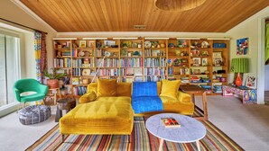 A cozy living room with a yellow sofa, a bookshelf filled with books, and a striped rug.