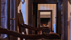 A hallway leading to a room with a fireplace, wooden furniture, and a door with a brass handle.