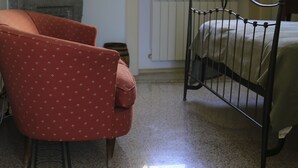 Una camera da letto con un letto, una poltrona rossa, un termosifone e una finestra vista alberi.