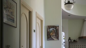 Un corridoio con una pianta in vaso, un frigorifero bianco e una porta che dà su un'altra stanza.