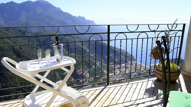 Un balcone con un tavolo bianco apparecchiato con bicchieri e una bottiglia, una sedia verde e una pianta in vaso.