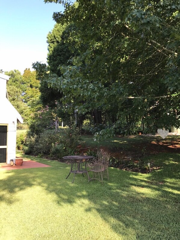 A backyard with a patio table and chairs, surrounded by lush greenery and a large tree.