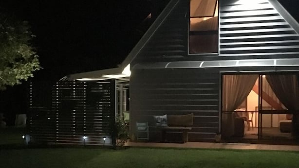 Uma casa moderna de dois andares com um amplo alpendre aberto e portas de correr que dão para o interior.