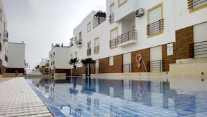 A swimming pool with a tiled edge, surrounded by multi-story buildings with balconies and windows.