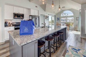Une cuisine moderne dotée de plans de travail en granit, d’appareils électroménagers en acier inoxydable et d’un grand îlot central avec des tabourets de bar.
