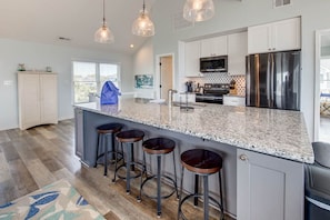 A kitchen with a granite countertop, stainless steel appliances, and bar stools.