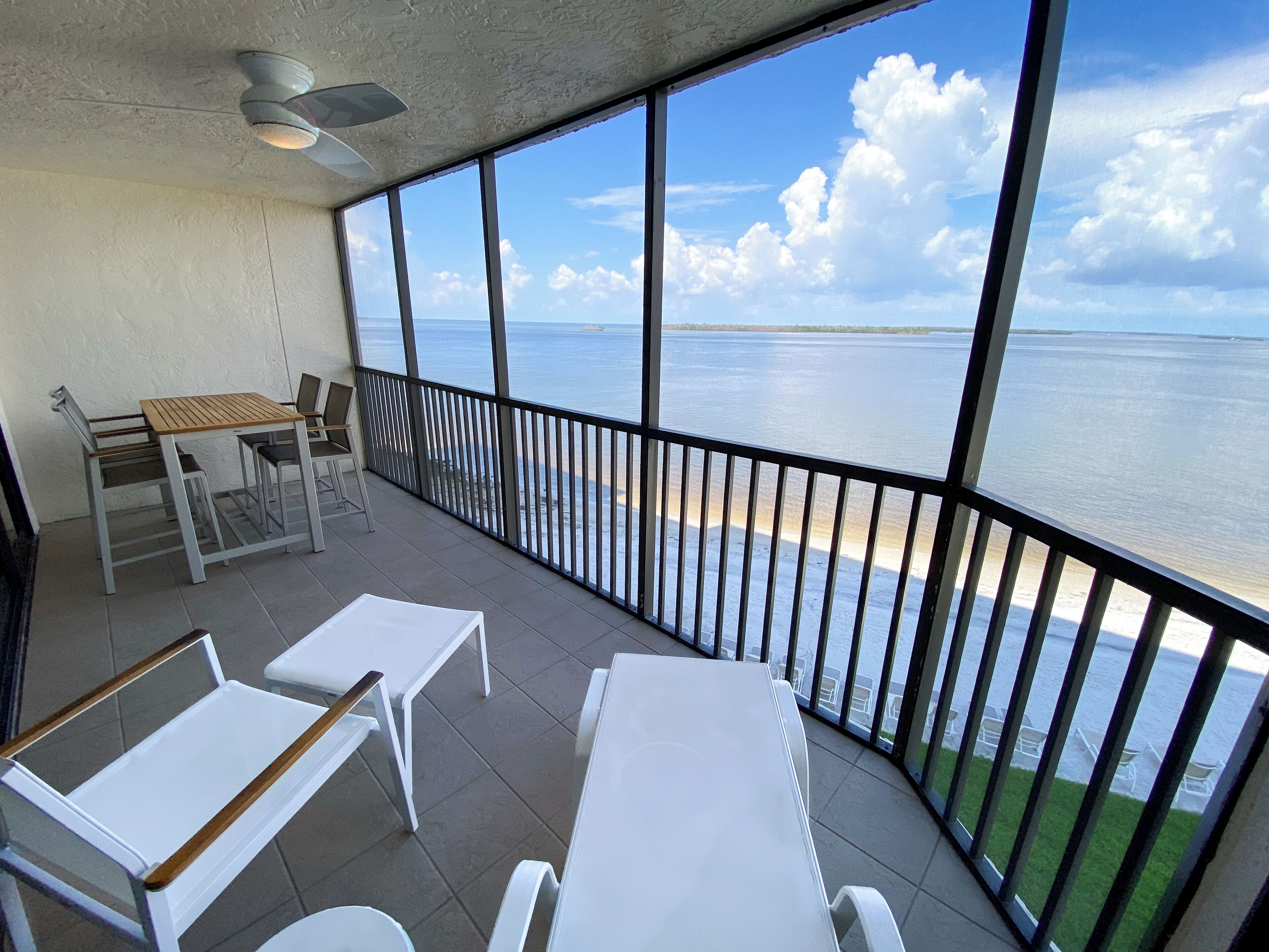A balcony with a view of the sea, a table, chairs, and a ceiling fan.