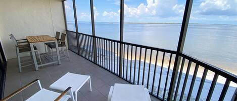 A balcony with a view of the sea, a table, chairs, and a ceiling fan.