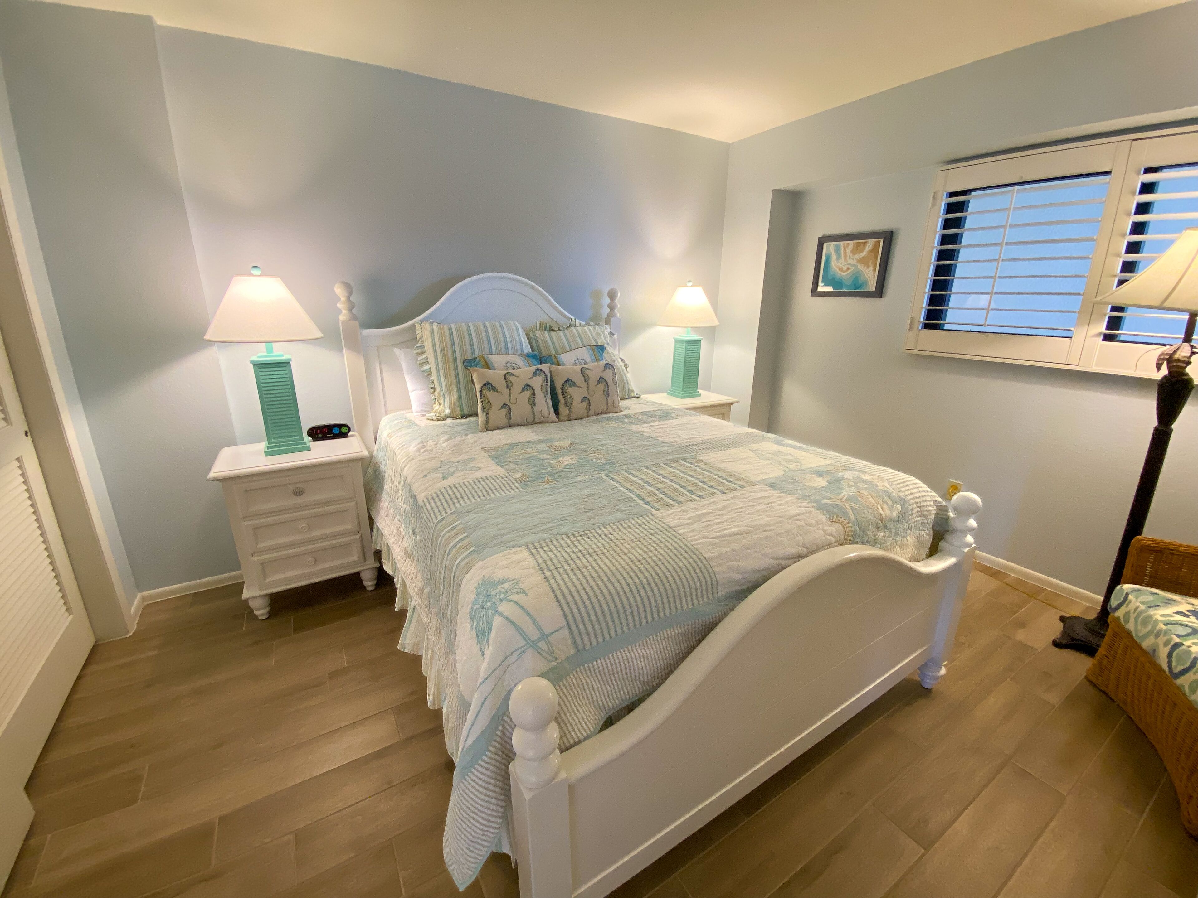 A bedroom with a bed, nightstands, a window with blinds, and a wall-mounted picture.