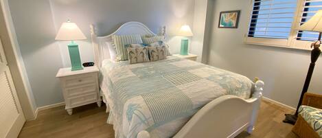 A bedroom with a bed, nightstands, a window with blinds, and a wall-mounted picture.