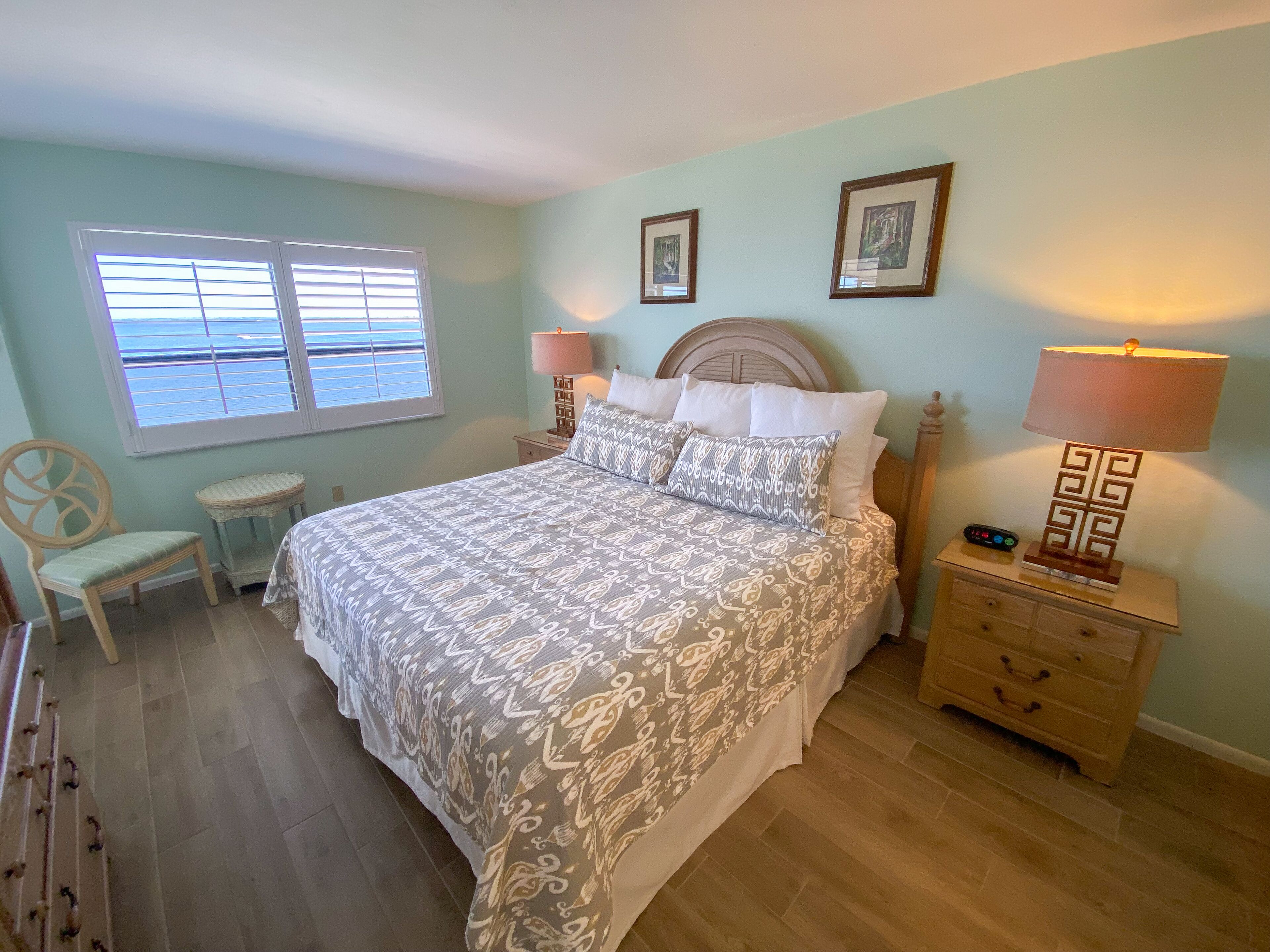 Une chambre bien rangée, avec un lit, des tables de chevet, une chaise et une fenêtre équipée de stores.