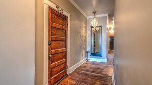 A hallway with a wooden door labeled "92-2", a chandelier, and a staircase in the background. - Historic Midtown Getaway | Close to Beale (Memphis)
