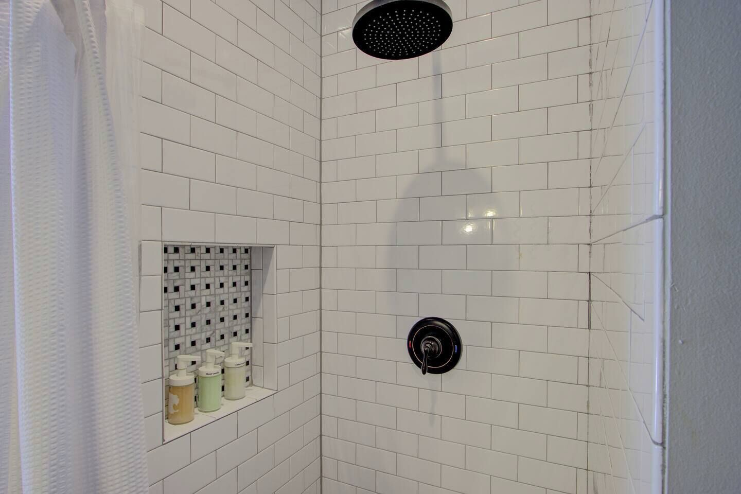 A shower with white tiles, a black showerhead, and a small shelf with toiletries.
