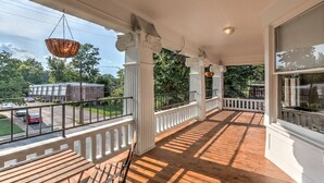 A covered porch with wooden flooring, white railings, and columns. - Historic Midtown Getaway | Close to Beale (Memphis)