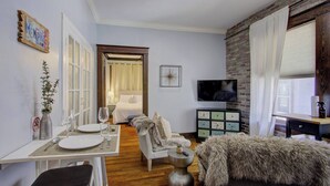 A hotel room with a bed, a TV, a desk with a chair, a dining table with a chair, and a fur throw on the sofa. - Historic Midtown Getaway | Close to Beale (Memphis)