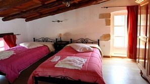 A bedroom with two beds, each with pink bedding and white pillows. There is a wooden ceiling and a window with red curtains. - Rock House's Villa Melody (2 Bedrooms, Sleeps 4) with private garden and pool. (Platanias)