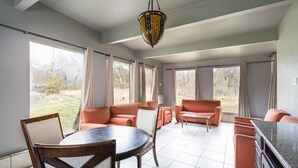 Un salón espacioso con una mesa redonda y asientos color naranja, ventanas grandes y una lámpara colgante.