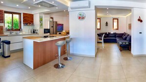 A modern kitchen with a central island, bar stools, and a dining area with a sofa. - Charming  Villa, quiet location, stunning view and infinity pool is all you need (Ražanj)