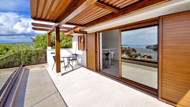 A modern balcony with a wooden pergola, a glass door leading to a terrace, and a view of a coastal landscape. - Charming  Villa, quiet location, stunning view and infinity pool is all you need (Ražanj)