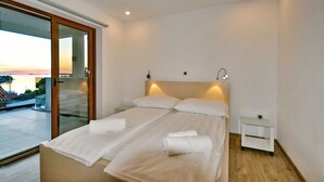 A double bed with two pillows and a bedside table with a lamp, in a room with a large window overlooking a balcony. - Charming  Villa, quiet location, stunning view and infinity pool is all you need (Ražanj)
