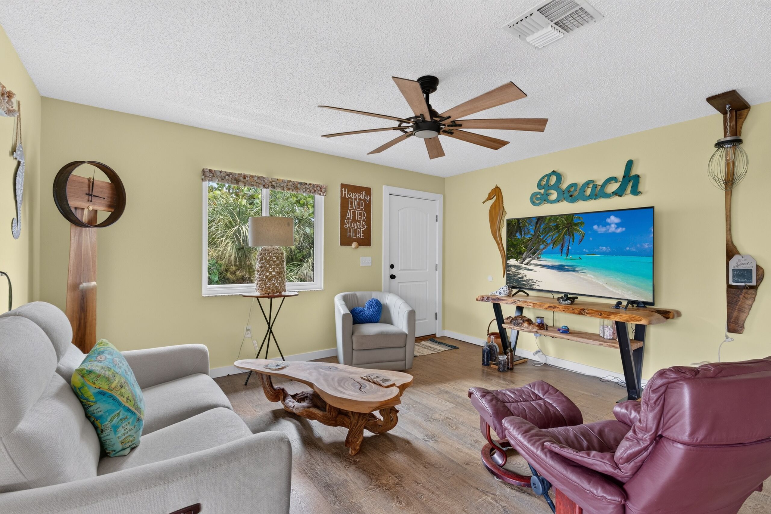 A living room with a ceiling fan, a television displaying a beach scene, a wooden coffee table, a sofa, and a leather recliner.