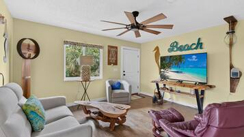 A living room with a ceiling fan, a television displaying a beach scene, a wooden coffee table, a sofa, and a leather recliner.