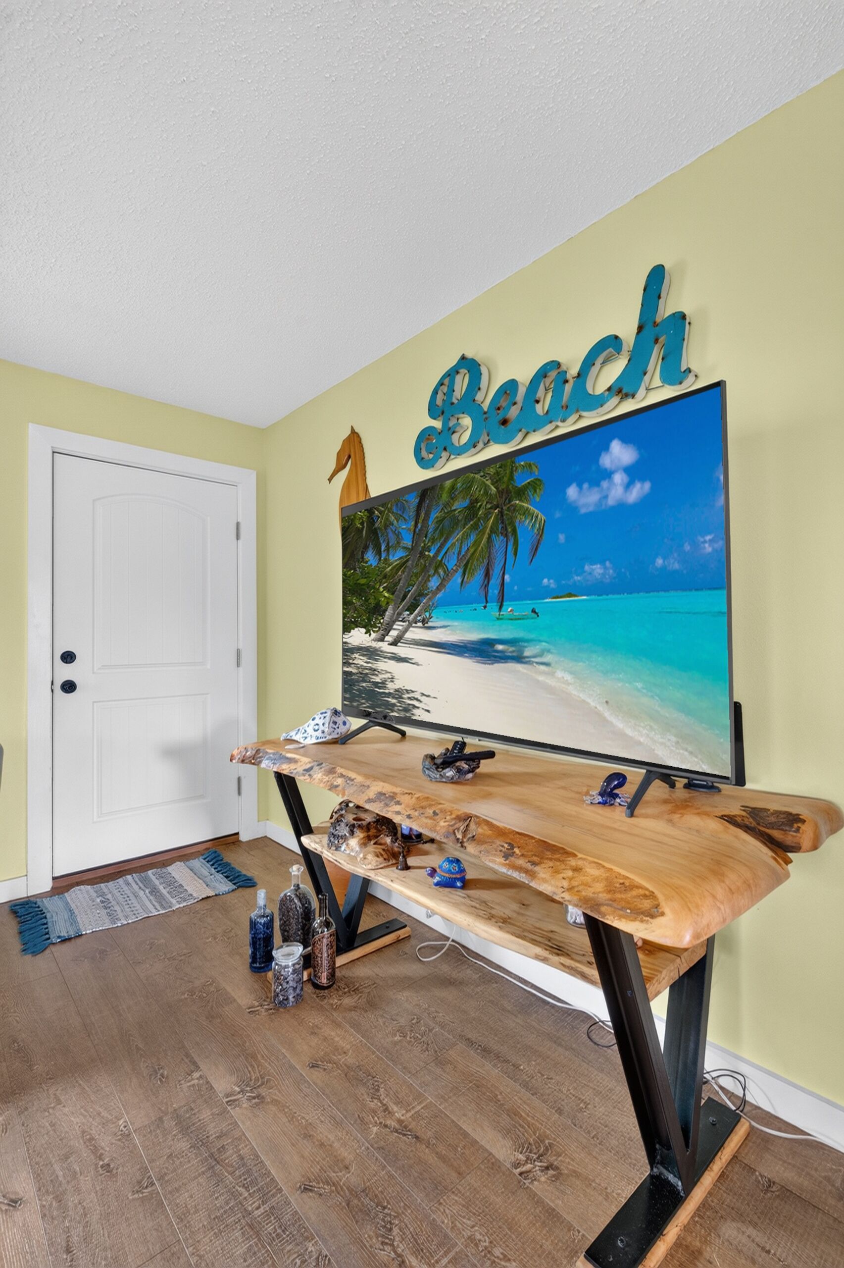 Ein Zimmer mit einem Holztisch, einem Strandbild und einer Tür.