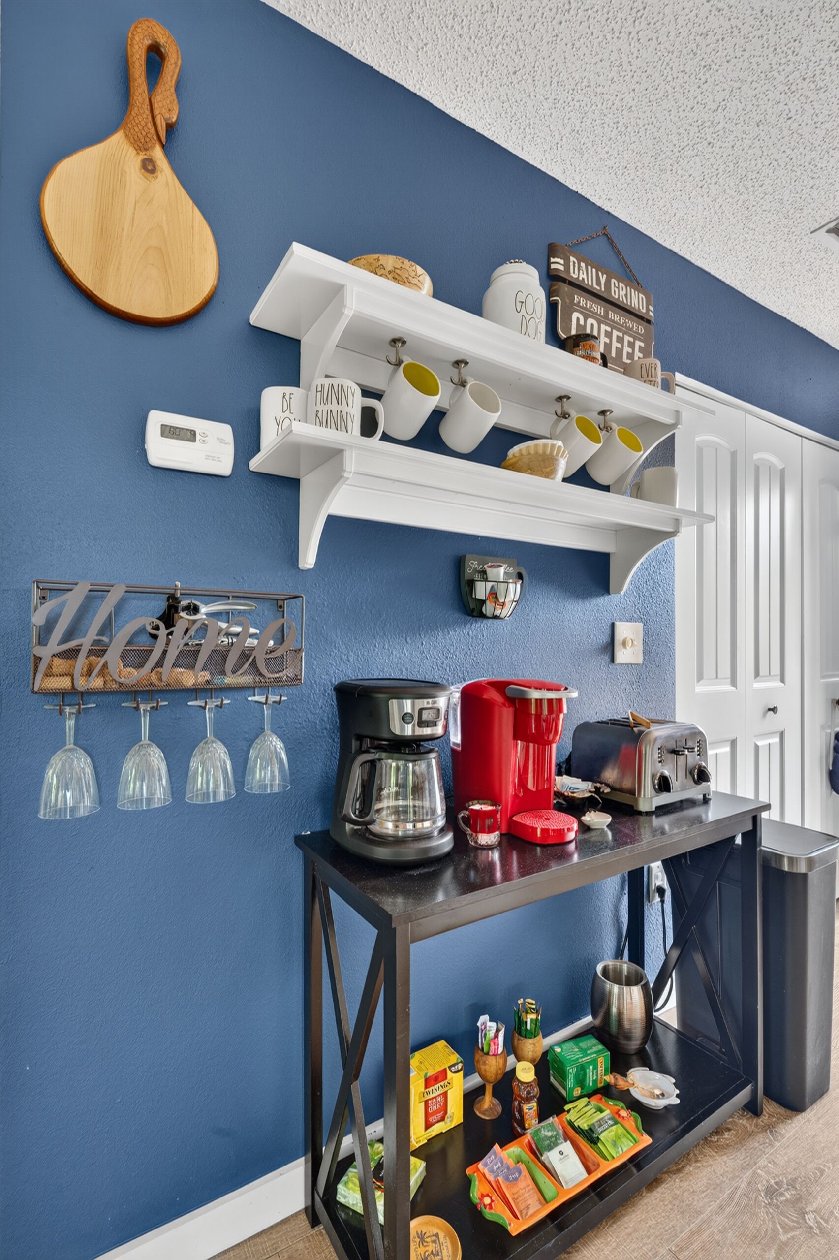 A kitchen with a blue wall, white shelves, and various kitchen appliances.