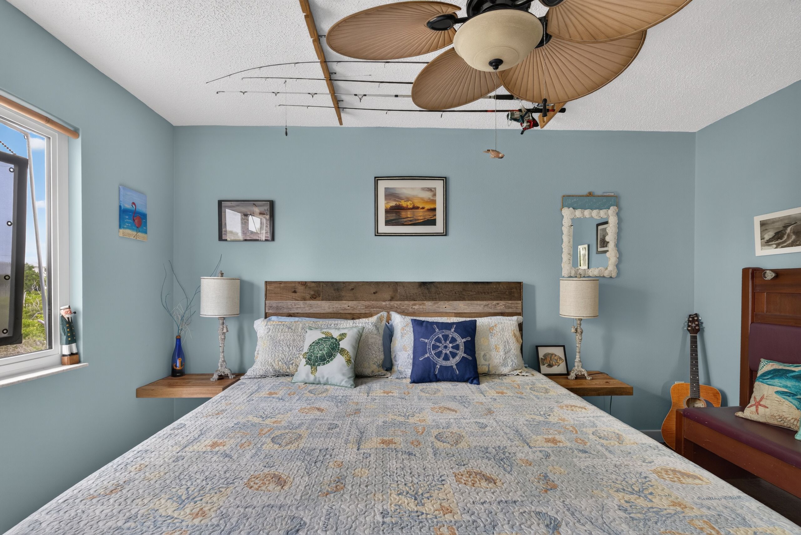 Ein Schlafzimmer mit Bett, Deckenventilator, Fenster und einer Gitarre.