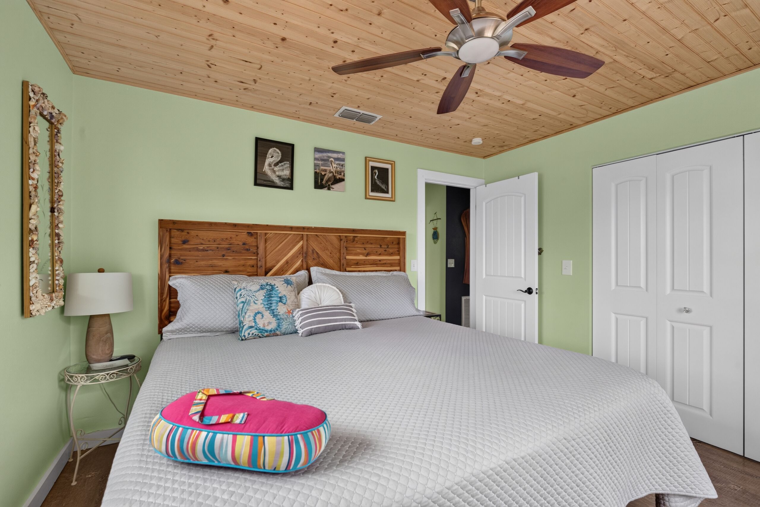 A bedroom with a wooden ceiling fan, a bed with a quilted bedspread, a bedside lamp, and a wall with framed pictures.