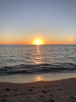 Ein Sonnenuntergang über einem ruhigen Meer mit sanften Wellen und einem Sandstrand.