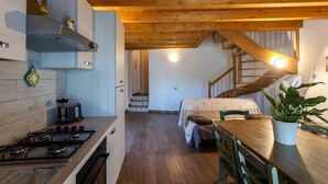 Una cocina con estufa, armarios y techo de madera. Se ve una escalera que conduce a otra habitación.
