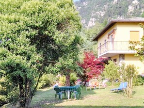 Un jardin avec une table et des chaises, un bâtiment doté d’un balcon et une montagne en arrière-plan.