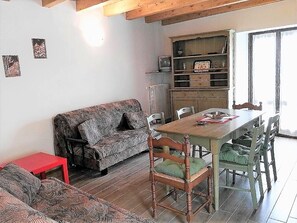 Un salon chaleureux avec un canapé à motifs, une table à manger avec des chaises et une petite table d’appoint rouge.