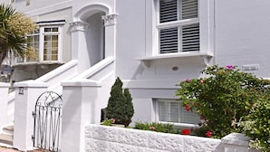 A white building with a gated entrance, a small staircase, and a well-maintained garden with various plants and flowers.