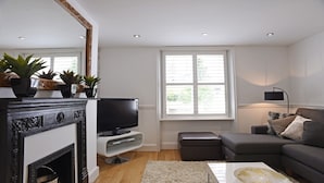 A living room with a fireplace, television, sofa, and a large window with blinds.